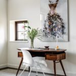 Office featuring painting of a dress above a dark wood midcentury desk and a white office chair with a furry seat