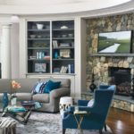 Family room featuring blue chair, gray couch with blue throw pillows, book shelves, stone fireplace, circular rug