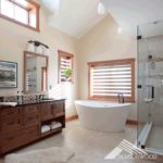 Master bathrooms with dark-wood vanity, large, white, stand-alone bathtub, and a glass shower. There are three wood-framed windows in the room, letting in plenty of natural light.