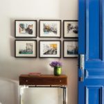 Blue door opens to an entryway featuring a brown side with an Hermes change tray and a vase of flowers. Above the table are six prints featuring Brooklyn scenes