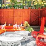 The back patio featuring an orange fence, orange high-backed chairs, a couch with orange cushions and three round white tables