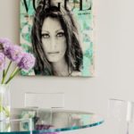 A painting of Sophia Loren on the cover of Vogue magazine hangs above a dining room table with purple chair cushions