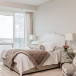 Master bedroom with bedding in shades of white and taupe. There's a view of Boston Harbor outside the window.