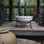 A bowl-shaped planter displayed in a black iron stand on a deck surrounded by forest