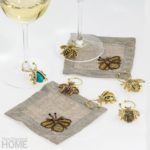 Natural-colored cocktail napkins surrounded by gold wine charms in the shape of bees and other flying insects
