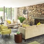 Living room with a stone fireplace, floor-to-ceiling windows, two tan couches, two lime green accent chairs, and walnut tables.