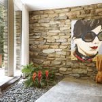 Living room with an in-ground planter featuring tropical plants. Behind the planter is a stone wall with a large painting of a woman in sunglasses.
