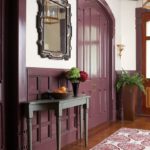 Entryway with purple doors, wainscotting and trim. There's a wood floor with a patterned rug and an accent table in dark gray.