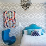 Bedrooms with a colorful blue headboard and a white duvet with blue accent pillows. There's a dark blue chair next to the bed and the wall is covered in gray and white geometric wall paper.