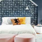 A bed with white coverings against a wall papered with navy and white geometric wall paper