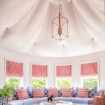 a fabric, tented ceiling in a round room with built-in seating below windows dressed in pink and white roman shades.