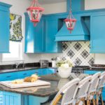 Blue kitchen cabinets with red lanterns hanging above an eat-in island surrounded by blue-and-white French bistro chairs