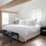 Bedroom with wood floors, white bedding, white walls and wood beams