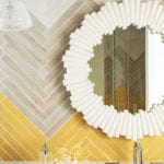 Bathroom with yellow and gray chevron tile and white mirror.