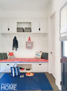 white mudroom with red upholstered bench and blue rug.