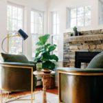 Two leather and brass chairs in front of a stone fireplace.