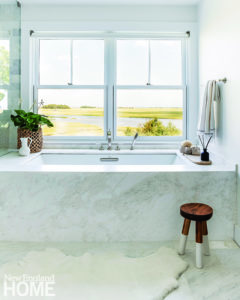 Bath tub placed under a window and surrounded by marble.