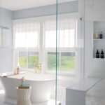 White soaking tub placed in front of a window with a coastal view.