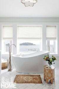 White freestanding bathtub in front of three windows.