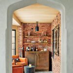 Cozy garden room with brick lined walls with a bronze bar and floating shelves.