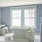 Free standing bathtub in a bathroom with blue and white patterned wall paper.