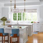 All-white kitchen with two kitchen islands and bright blue stools.