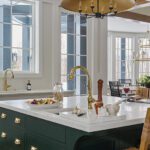 Green kitchen island with a large brass and black chandelier