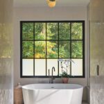 White freestanding tub in front of a large black framed window