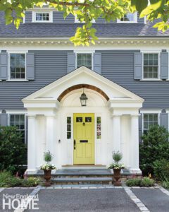 Exterior of a colonial home with gray siding and a yellow door.