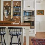 Kitchen island topped with walnut and a glass front cabinet