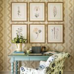 Work space with a small light blue desk, floral upholstered chair, and a beige and white wallpaper.