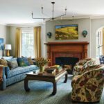 Living room in a historic home with a fireplace with a wooden surround and a blue couch and floral upholstered chairs