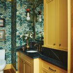 Powder room with yellow cabinetry and leafy patterned wallpaper