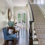 Entryway with white panelled walls, blue chairs, and a beige stair runner