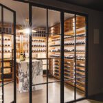 Luxurious home wine cellar with glass doors, illuminated wooden shelves displaying wine bottles, and a marble tasting table, creating an elegant, modern ambiance.