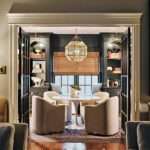 Elegant seating area with cozy armchairs around a round table, surrounded by dark built-in shelves, decorative accents, and a gold geometric chandelier for a sophisticated ambiance.