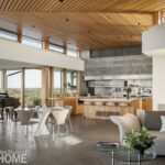 Open-concept modern kitchen and dining area featuring a sleek concrete accent wall, wood-paneled ceiling, large island with bar seating, glass dining table, and floor-to-ceiling windows with panoramic outdoor views.