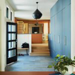 Modern entryway with sleek blue cabinetry, black pendant light, and a glass-panel front door opening to a bright, minimalist interior design.