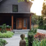 Contemporary home exterior with a dark facade, warm wooden accents, and lush landscaping leading to a modern front entrance.