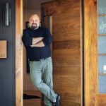 David Boronkay standing at the entrance of his home, leaning against a rich wooden door framed by a sleek black facade.