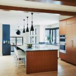 Contemporary kitchen design with a large central island, wood cabinetry, and bold black pendant lights creating a bright and functional space.