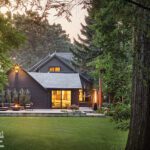 Striking rear exterior of a contemporary home at twilight, with illuminated interiors and a spacious patio surrounded by greenery.