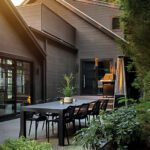 Elegant outdoor dining area with a sleek black table, modern chairs, and lush greenery, creating a serene al fresco setting.
