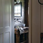 Rustic powder room featuring a reclaimed wood vanity, a stone sink, a brick accent wall, and a black-framed mirror, blending vintage charm with modern functionality.