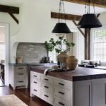 Rustic kitchen with exposed wooden beams, a large butcher block island, cream cabinetry, and a brick backsplash, offering a warm and functional space for cooking.