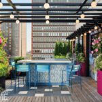 Sophisticated outdoor bar area with contemporary barstools, a sleek counter, and hanging lights under a pergola on a Boston rooftop.