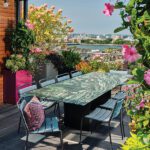Rooftop dining area with a green marble table, chic chairs, and vibrant flowers, offering scenic views of Boston and the river.