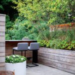 Modern home bar with minimalist wood and stone accents, ambient lighting, and sleek seating for a tranquil social space.