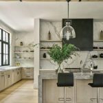 Sleek modern kitchen with marble waterfall island, light oak cabinetry, black hood range, and natural wood accents beneath exposed ceiling beams.