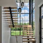 Architectural floating staircase with light wood treads and black metal accents, framed by double-height windows that fill the space with natural light.